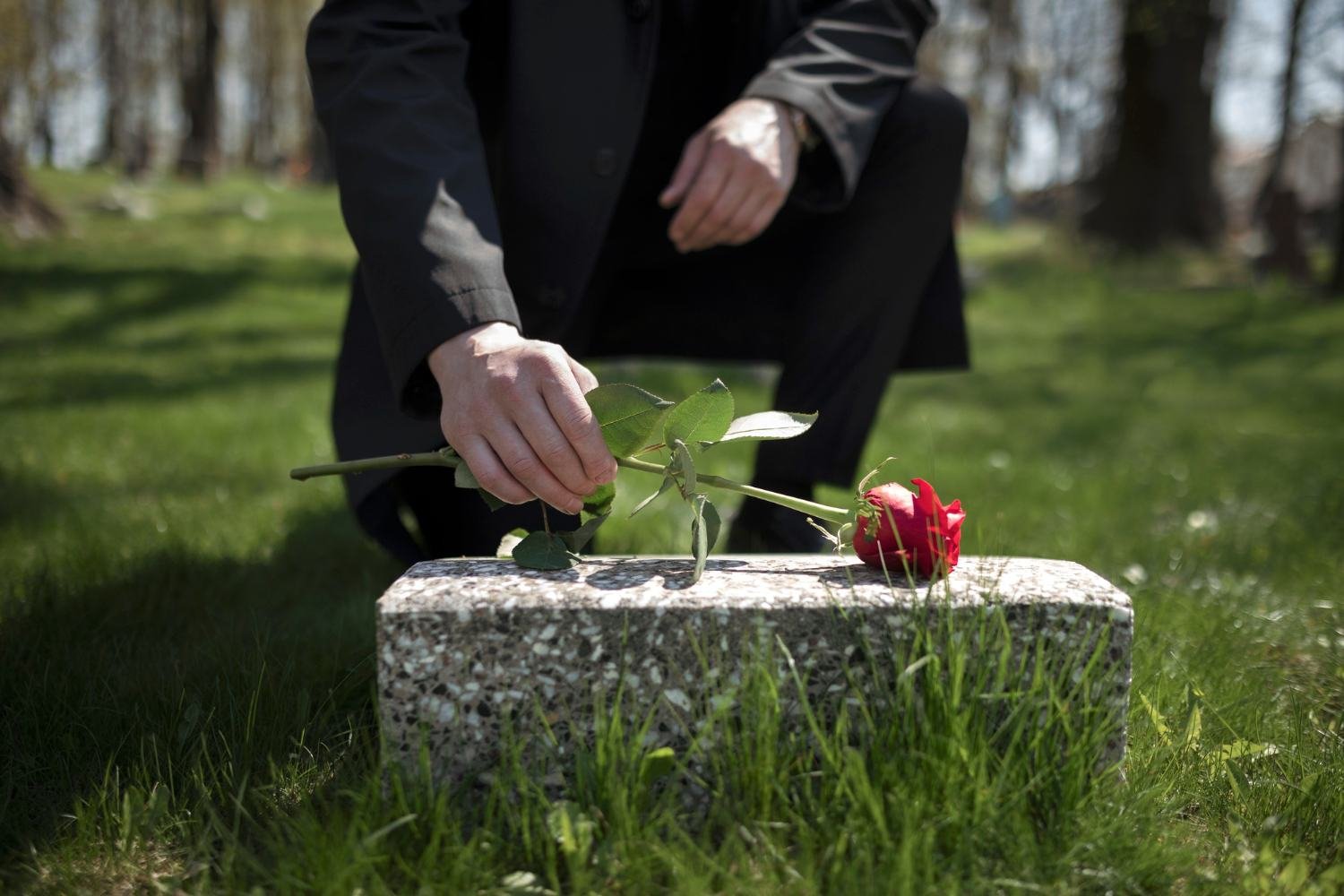 Man bringing a rose to a tombstone at the cemetery